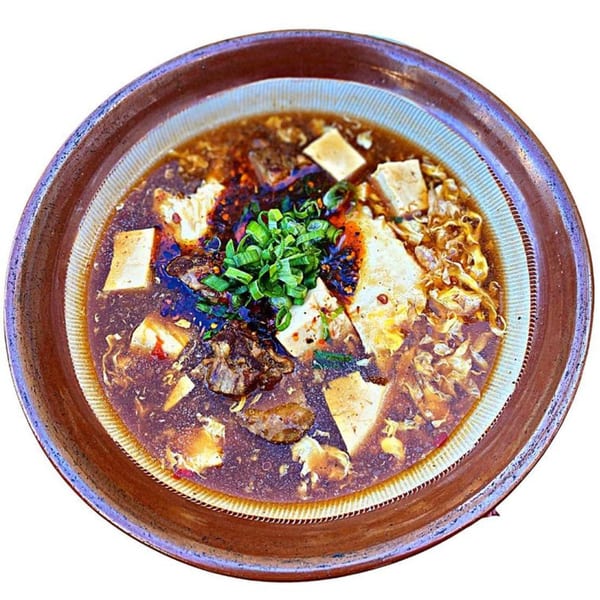 A bowl of Sapporo Ramen with tofu, meat, and green onions in a rich broth.