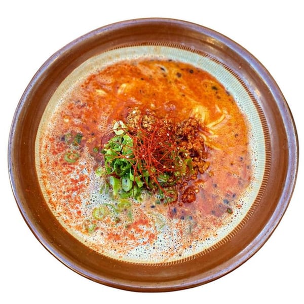 Spicy Sapporo ramen with ground meat, green onions, and red chili threads in a brown bowl.