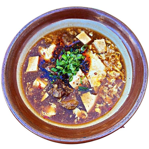 A bowl of Sapporo Ramen with tofu, meat, and green onions in a rich broth.