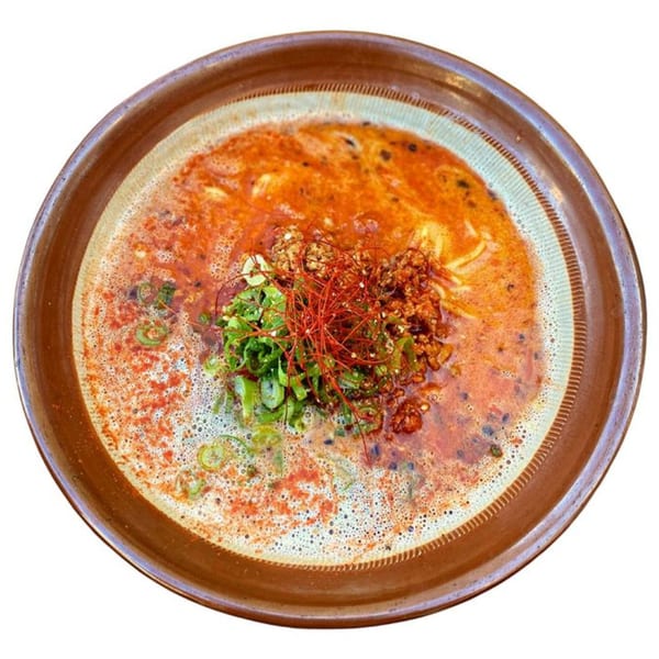 Spicy Sapporo ramen with ground meat, green onions, and red chili threads in a brown bowl.